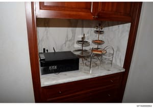 This is a photograph of a built-in display cabinet with a marble interior containing electronics and decorative objects. The cabinet features a black audio receiver/amplifier on the left side and multiple tiered metal stands with decorative items on 