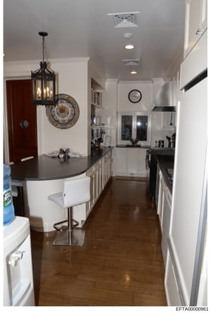 This is a photograph of a luxury kitchen interior featuring contemporary design elements including a curved black countertop island with white seating, white cabinetry, black stainless steel appliances, decorative pendant lighting, and hardwood floor