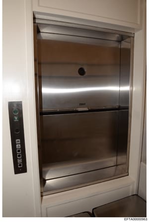 This photograph shows a stainless steel elevator installed within a residential building. The image captures the elevator doors, control panel, and interior finishes, likely documenting property features or conditions relevant to the investigation.