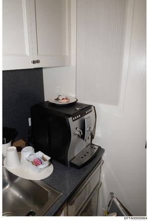 This is a photograph of a kitchen area showing modern appliances and cabinetry, likely from one of Epstein's properties. The image displays a built-in espresso machine, white upper cabinets, dark countertops, and kitchen accessories including cups an