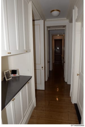 This is a photograph of an elegant hallway in what appears to be one of Jeffrey Epstein's residences, showing white paneled cabinetry, dark wood flooring, brass fixtures, and multiple doorways. The image documents the interior architectural design an