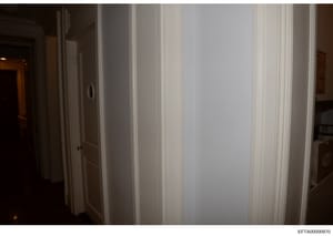 This is an evidence photograph showing an interior hallway with white paneled doors and cream-colored walls with decorative molding. The photo appears to be taken in a residential property, likely one of Epstein's residences. The hallway is dimly lit