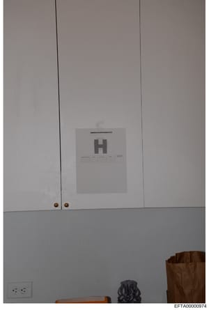 This is a photograph of an interior space showing white cabinetry with brass knobs and white walls. A measurement scale card marked with the letter 'H' is positioned in the center of the image for reference purposes, commonly used in forensic or evid