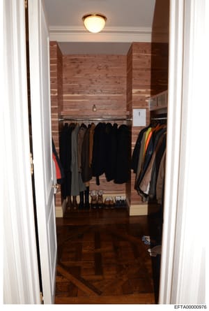 This is a photograph of a residential walk-in closet showing multiple clothing items on hanging racks and shoes arranged on the floor. The closet features wooden walls, recessed lighting, and contains primarily dark-colored outerwear and jackets. Thi