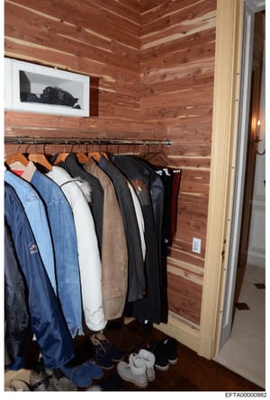 This is a photograph of a residential closet interior showing wooden cedar-lined walls with various clothing items on hangers, shoes on the floor, and what appears to be electronic equipment mounted on the wall. The photo documents the interior space