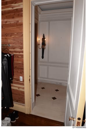 This is a photograph of an interior room space showing a walk-in closet or dressing area with cedar wood paneling on the left wall, white painted cabinetry with decorative hardware, and light tile flooring with dark accent tiles. The space contains c