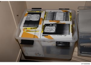 This photograph documents the physical storage and preservation of computer hard drives seized as evidence in the Epstein investigation. Multiple PATA/IDE hard drives are shown stored in clear plastic evidence containers with yellow 'EVIDENCE' labels
