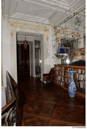 This is a photograph of a luxuriously appointed hallway or gallery space within what appears to be an upscale residence. The image shows classical architectural details including ornate gold-trimmed ceiling moldings, white walls with detailed framing