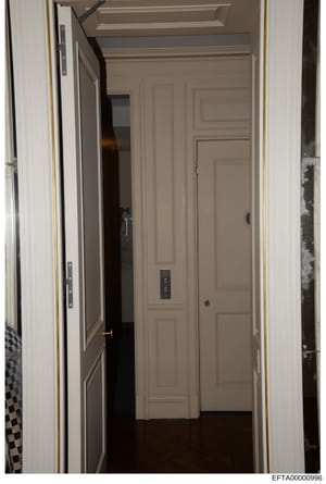 This photograph shows an interior hallway featuring a modern elevator installation within what appears to be a residential property. The image captures the elevator door, frame, and surrounding hallway architecture with paneled walls and white trim. 