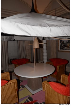This is a photograph of a modern interior seating area under a large white canopy or tent-like ceiling structure. The room features a round white table with wicker chairs upholstered in red cushions, draped curtains in neutral tones, and decorative e