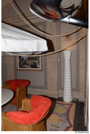 This is an evidence photograph showing the interior of a bedroom featuring distinctive design elements including patterned wallpaper, red upholstered furniture with wooden frames, a white cylindrical column, and a circular mirror with rope detailing.