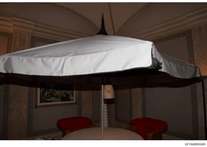 This is a photograph of an interior room showing a four-poster canopy bed with white fabric draping and black frame, flanked by two red upholstered benches. The room features damask wallpaper, ornate architectural details, and classical furnishings. 