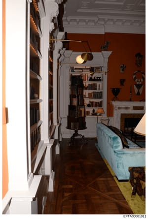 This photograph shows an interior room from what appears to be a luxury residence, featuring built-in bookshelves, a fireplace, decorative African or tribal art pieces, and period furnishings. The room displays a sophisticated design aesthetic with t