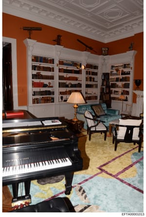 This is a photograph of a luxurious residential interior space, likely from one of Epstein's properties, featuring a grand piano, extensive built-in bookshelves, and high-end furnishings. The room displays significant wealth through its architectural