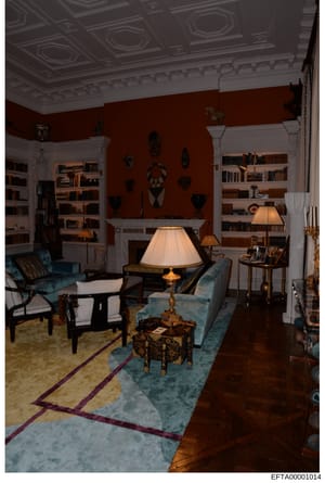 This is an evidence photograph showing a formal living room interior with distinctive décor. The room features rust/terracotta-colored walls, ornate white crown molding and ceiling details, built-in white bookshelves, blue upholstered furniture, Afri