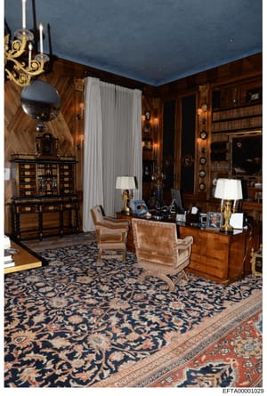 This photograph documents a lavishly decorated interior room featuring dark wood paneling, ornate furniture, and high-end décor. The room includes an ornamental desk, decorative cabinets, period furniture, gilt-trimmed lamps, and elaborate architectu