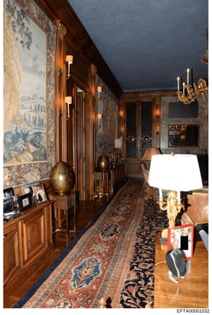 This photograph documents a hallway or corridor inside one of Jeffrey Epstein's properties, displaying high-end interior design including ornate wall paneling, classical artwork, expensive lighting fixtures, and fine furnishings. The image serves as 