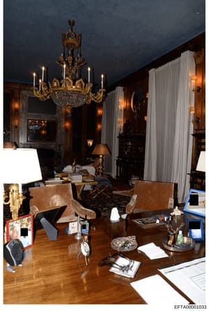 This is a photograph of an elegantly decorated office or study room featuring high-end furnishings, ornate décor, and luxury appointments. The room displays a gold-trimmed chandelier, wood paneling, marble fireplace, period furniture, and various per