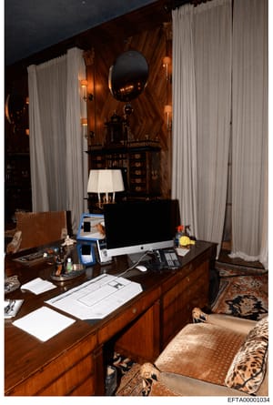 This photograph shows a luxuriously appointed interior room featuring a wooden desk with modern computer equipment, ornate furnishings, and detailed décor. The room displays high-end styling with rich wood paneling, heavy curtains, decorative mirrors