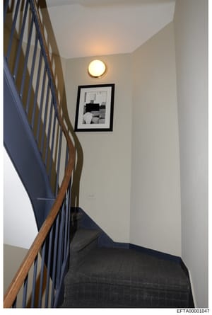 This is a photograph of an interior stairwell, showing a modern residential space with wooden handrails, metal balusters, recessed lighting, and framed artwork on the wall. The image appears to be documentation of a property, likely one of Jeffrey Ep