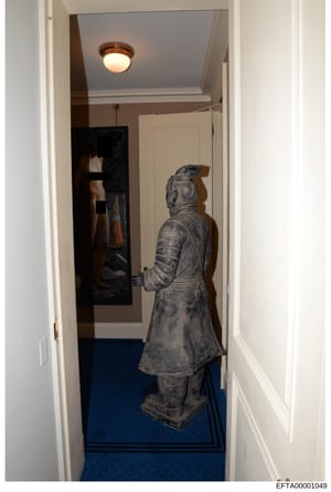 This photograph shows an interior hallway in what appears to be a residential property, featuring a gray stone or resin statue of an Asian figure in traditional clothing positioned in the corridor. The image documents the interior décor and furnishin