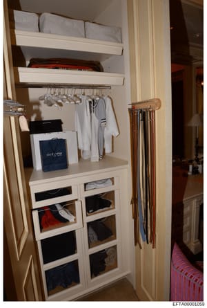 This photograph shows a built-in closet from what appears to be a residential property, displaying organized clothing storage with shelving, drawers, and hanging space. The closet contains various garments including white clothing, striped items, and