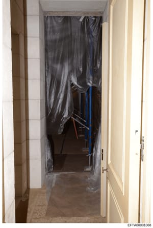 This photograph shows an interior hallway or passageway covered with black plastic sheeting, suggesting renovation, containment, or evidence preservation work. The plastic-covered area contains metal scaffolding or support structures visible in the b