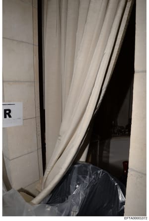 This is an evidence photograph from a property search or inspection, showing an interior doorway with cream-colored curtains and a dark object (possibly covered item or furniture) on the floor. An evidence marker labeled 'R' is visible on the left wa