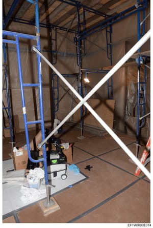 This is an evidence photograph showing the interior of a property under construction or renovation, featuring blue metal scaffolding, white bracing, construction materials, and work equipment. The image appears to be part of property documentation re