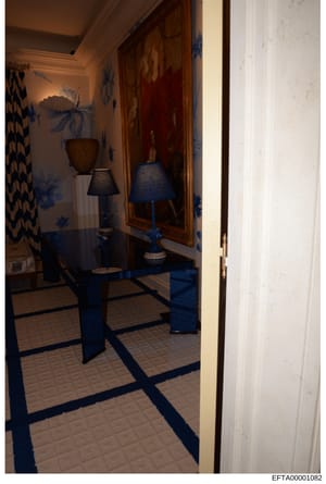 This is a photograph of an interior room, likely from one of Jeffrey Epstein's properties, showing a decorative space with blue and white floral wallpaper, elegant furnishings including a dark table with lamps, and patterned flooring. The image appea