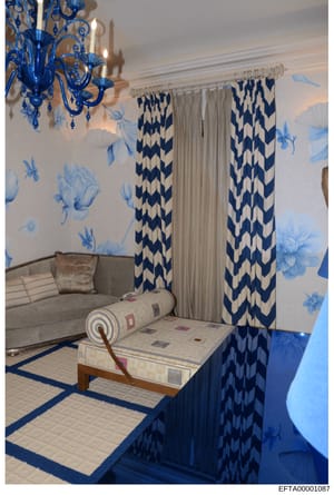 This is a photograph of an elegantly decorated interior space featuring blue and white color scheme with custom furnishings, wallpaper, curtains, and a statement chandelier. The image appears to be documentation of interior design or property decorat