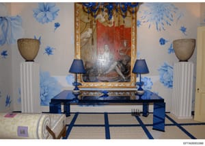 This is a photograph of an elegantly decorated interior room featuring blue and white Chinoiserie-style wall treatments, a central display table with classical framed artwork above it, and coordinating decorative elements. The room appears to be part