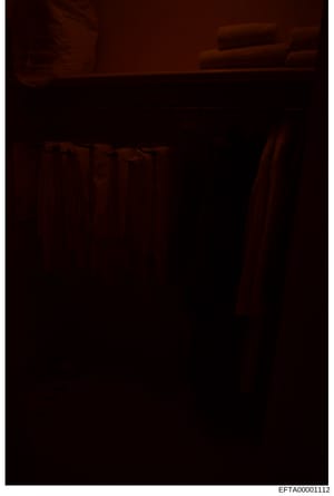 This is a photograph of an interior room showing furniture in warm lighting conditions. The image is severely underexposed and difficult to interpret clearly, but appears to show a residential space with what looks like a bed frame and other furnishi