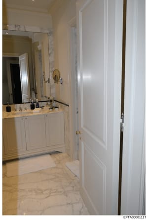 This is a photograph of an upscale bathroom interior featuring marble flooring, dual vanities with white cabinetry, large mirrors, and brass fixtures. The image appears to be documentation of property interiors, likely from one of Epstein's residence