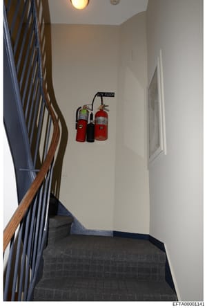 This is an evidence photograph showing the interior of a stairwell at one of Epstein's properties. The image depicts a landing with fire extinguishers mounted on the wall, labeled '3RD FLOOR'. The photograph documents the building's safety equipment 