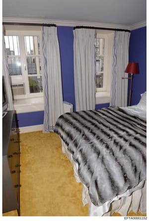 This is a photograph of a residential bedroom interior, likely from one of Epstein's properties. The room features distinctive blue walls, multiple large windows with light curtains, gold/tan carpeting, and contemporary furnishings. The photo appears