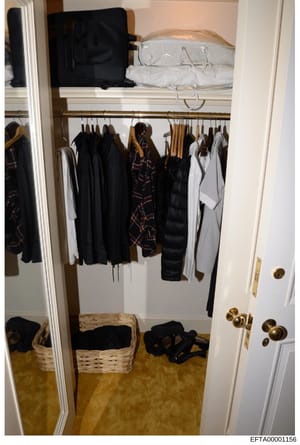 This is a photograph of a walk-in closet containing various clothing items, storage baskets, and personal belongings. The closet features a brass rod with multiple hangers holding predominantly black clothing items, some plaid/patterned pieces, white