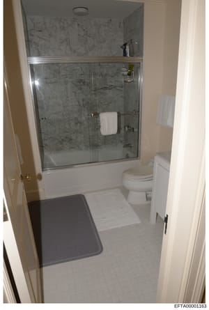 This is a photograph of a residential bathroom interior showing a walk-in shower with marble tile surround, a toilet, sink vanity, and tiled flooring. The image appears to be evidence documentation from a property inspection or inventory, likely take