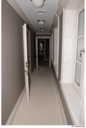 This is a photograph of an elegant residential hallway featuring white walls, brass fixtures, and multiple doorways. The image appears to be evidence documentation of one of Jeffrey Epstein's properties, showing the interior layout and architectural 