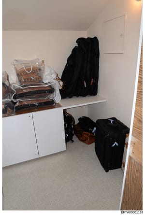 This is an evidence photograph of a residential closet space containing stored clothing, luggage, and personal items. The image shows a white shelving unit with folded garments in clear storage bags, black clothing hanging on the wall, and multiple b