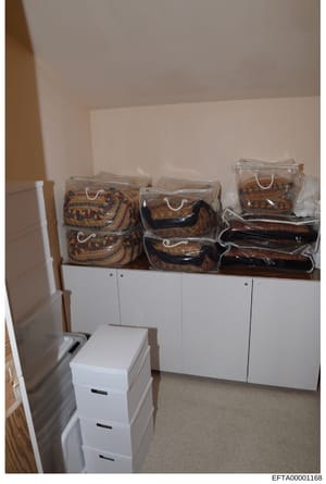 This photograph documents an interior storage or closet space containing multiple luxury designer handbags in clear plastic storage bags arranged on white cabinetry. The bags appear to be high-end merchandise with ornate patterns in brown, gold, and 