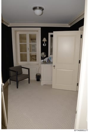 This is a photograph of an interior room featuring a modern design scheme with black accent walls, white trim, and contemporary furnishings. The image shows a doorway entrance, storage cabinets, wall sconces, and a chair, appearing to be part of evid
