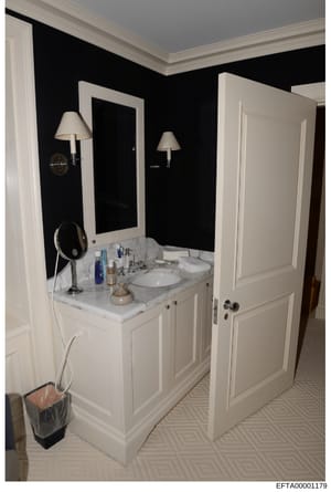 This is a photograph of a luxury bathroom interior, likely from one of Epstein's properties. The image shows a contemporary bathroom design with a white dual-sink marble vanity, black accent walls, white trim and molding, wall-mounted sconces, and mo