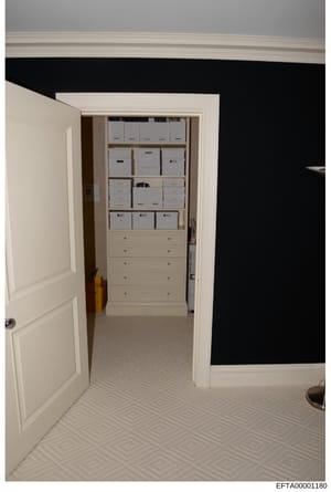 This is a photograph of a walk-in closet interior showing multiple white cardboard storage boxes organized on shelves and drawers. The closet features cream-colored cabinetry with a herringbone-pattern floor and black accent wall visible in the adjac