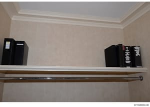 This is an evidence photograph showing a wall-mounted shelving unit containing multiple black binders and file boxes, each labeled with evidence tags or identification markers. The photo appears to be documentation of seized materials or physical evi