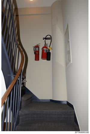 This is a photograph of an interior stairwell landing showing fire safety equipment mounted on the wall. Two red fire extinguishers and one black fire extinguisher are mounted below a '3rd Floor' sign. The image appears to be part of property documen
