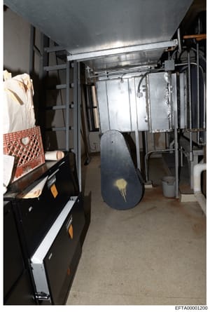 Photograph of an industrial or commercial storage room/basement space containing mechanical heating or cooling equipment, metal framing, building materials, and miscellaneous stored items. The image appears to be evidence documentation from a propert