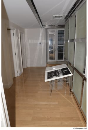 This is an evidence photograph showing a modern hallway interior with white walls, wood flooring, and contemporary design features. The image appears to be part of property documentation during the investigation, showing the layout and condition of i