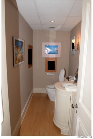 This is a photograph of a bathroom interior, likely from one of Jeffrey Epstein's properties. The image shows a renovated bathroom with contemporary fixtures and decor, including framed artwork on the walls. The photo appears to be documentation of t