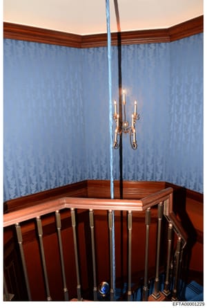 This is an evidence photograph showing the interior of a bedroom featuring a wooden crib with metal railings, decorative blue patterned wallpaper with a damask design, a dark wood wainscoting, and an ornate brass candelabra suspended from the ceiling